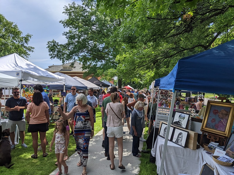People walking among booths with artwork in a park