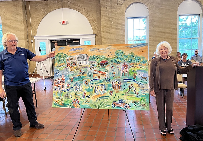 A man and a woman stand on either side of an unveiled painting depicting scenes of Fort Thomas, Kentucky