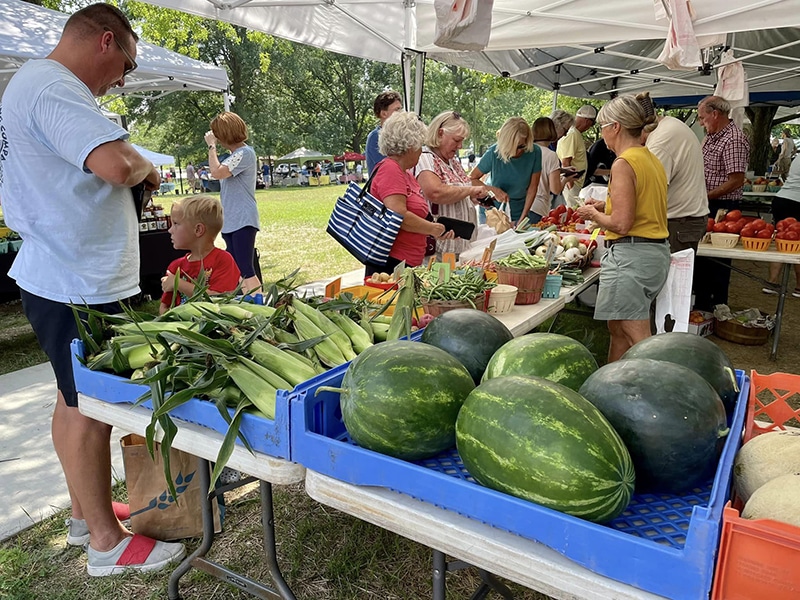 People at food stalls with watermelons, corn and other vegetables