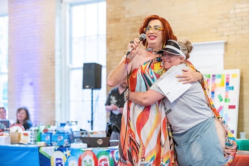 Drag performer on stage gets a hug from a fan.