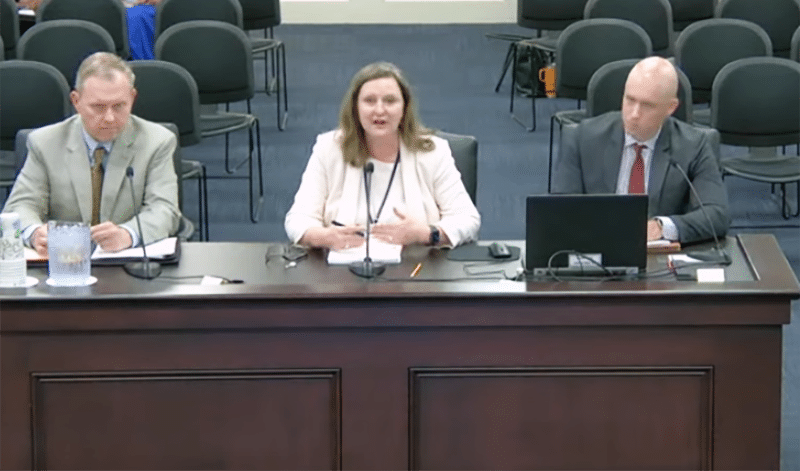 Three people at a desk speaking at a meeting.