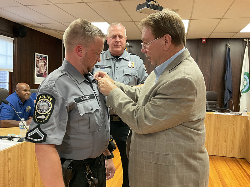 A man in a suit is pinning a badge on a police officer. Another officer is standing behind them.