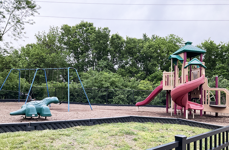 Park with slide, swings and plastic dinosaur for climbing.