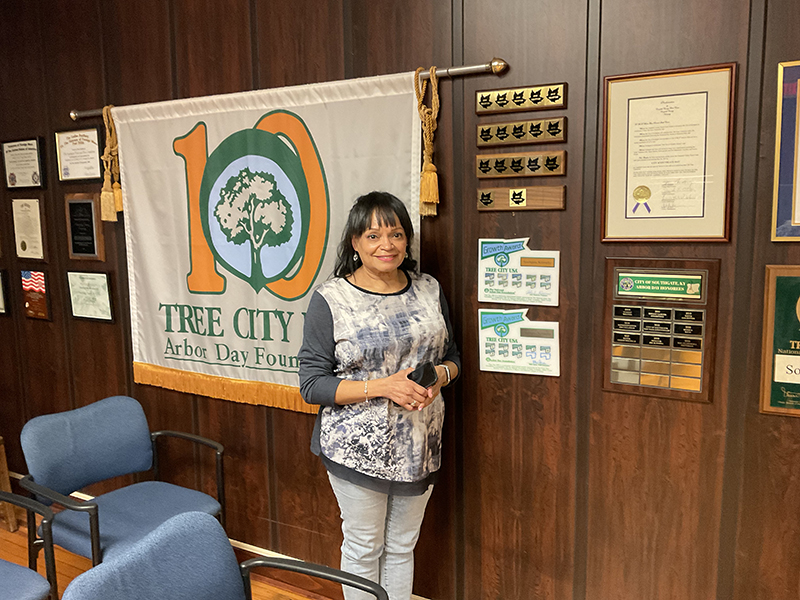 Woman stands in front of a banner reading "Tree City USA" and several plaques on the wall behind her.