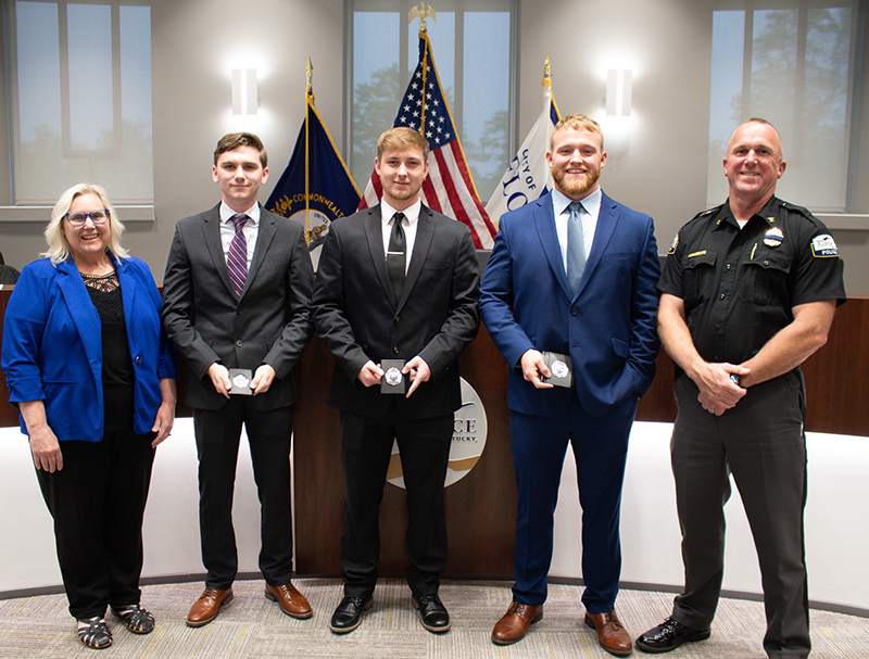 Five people stand in front of a dais with the American flag behind them. One is in police uniform.