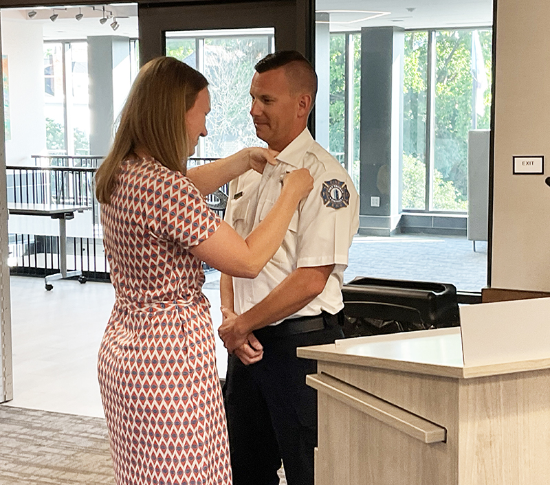 Woman pins badge on man in firefighter uniform. They are standing behind a podium.