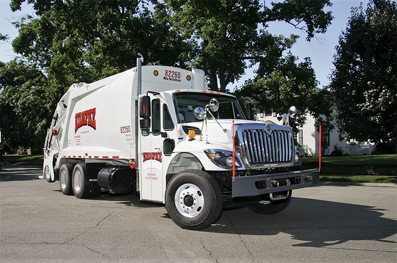 A large trash pick up truck in a parking lot.