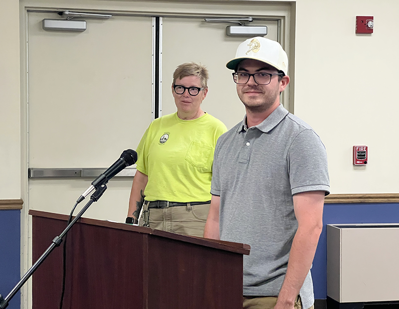 Man and woman stand at a podium. The woman is wearing a shirt indicating she is a member of the Bellevue Public Services Department.